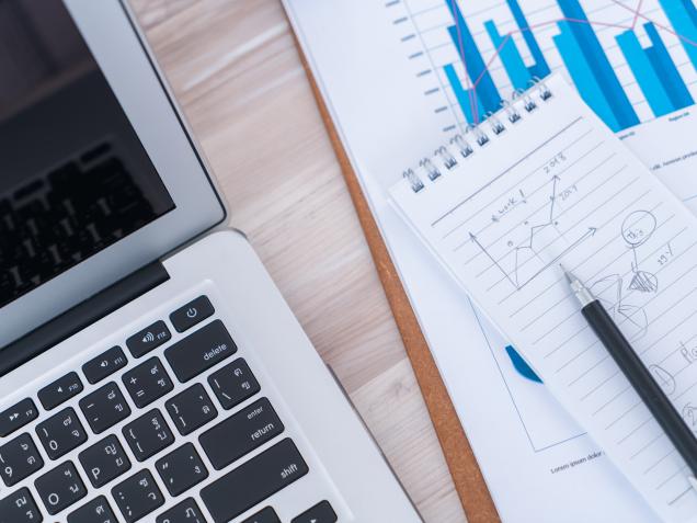 Ordinateur portable et documents financiers avec graphiques illustrant le suivi administratif et financier